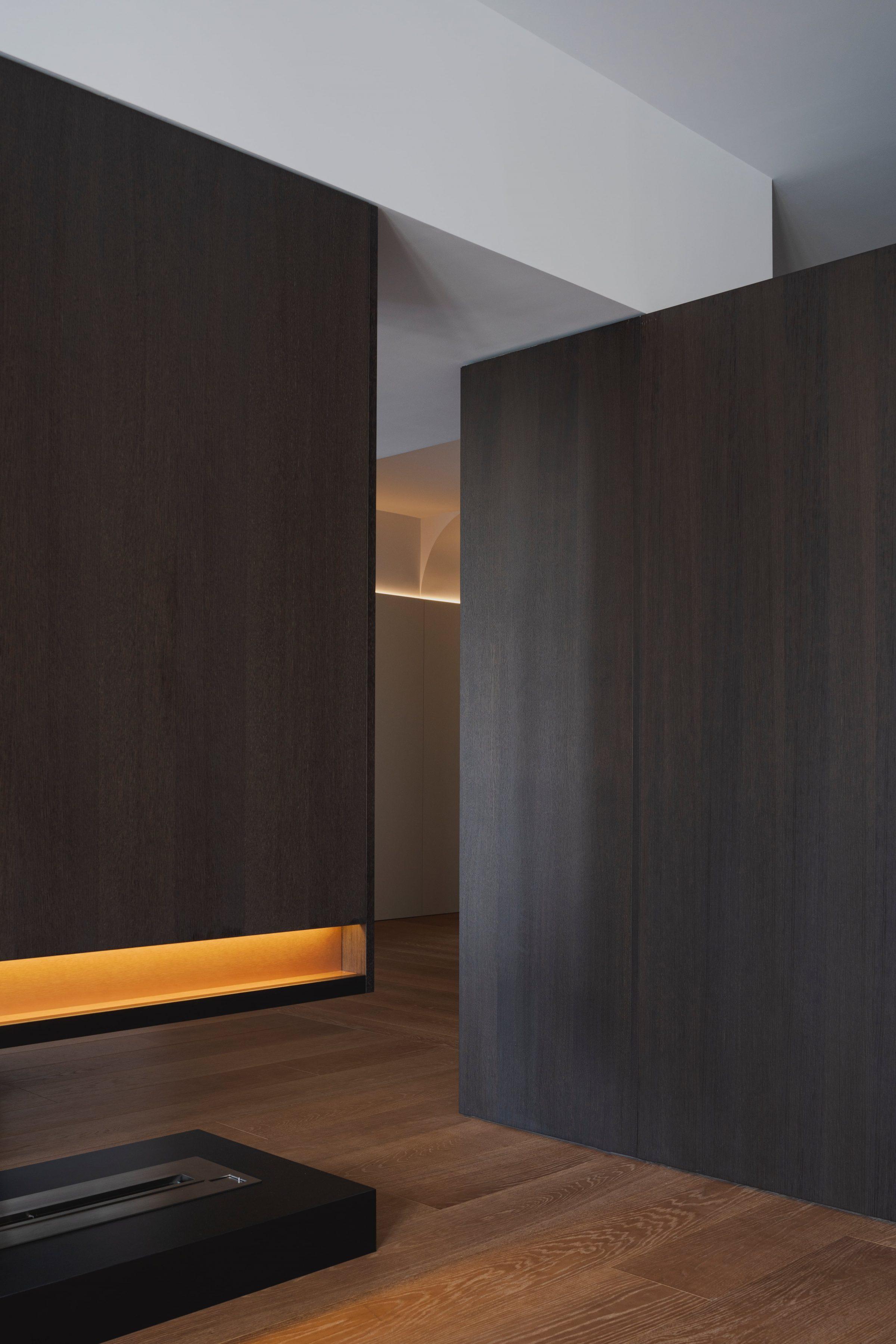 AO17 Apartment — dark walnut wall with copper-lit niche above the fireplace