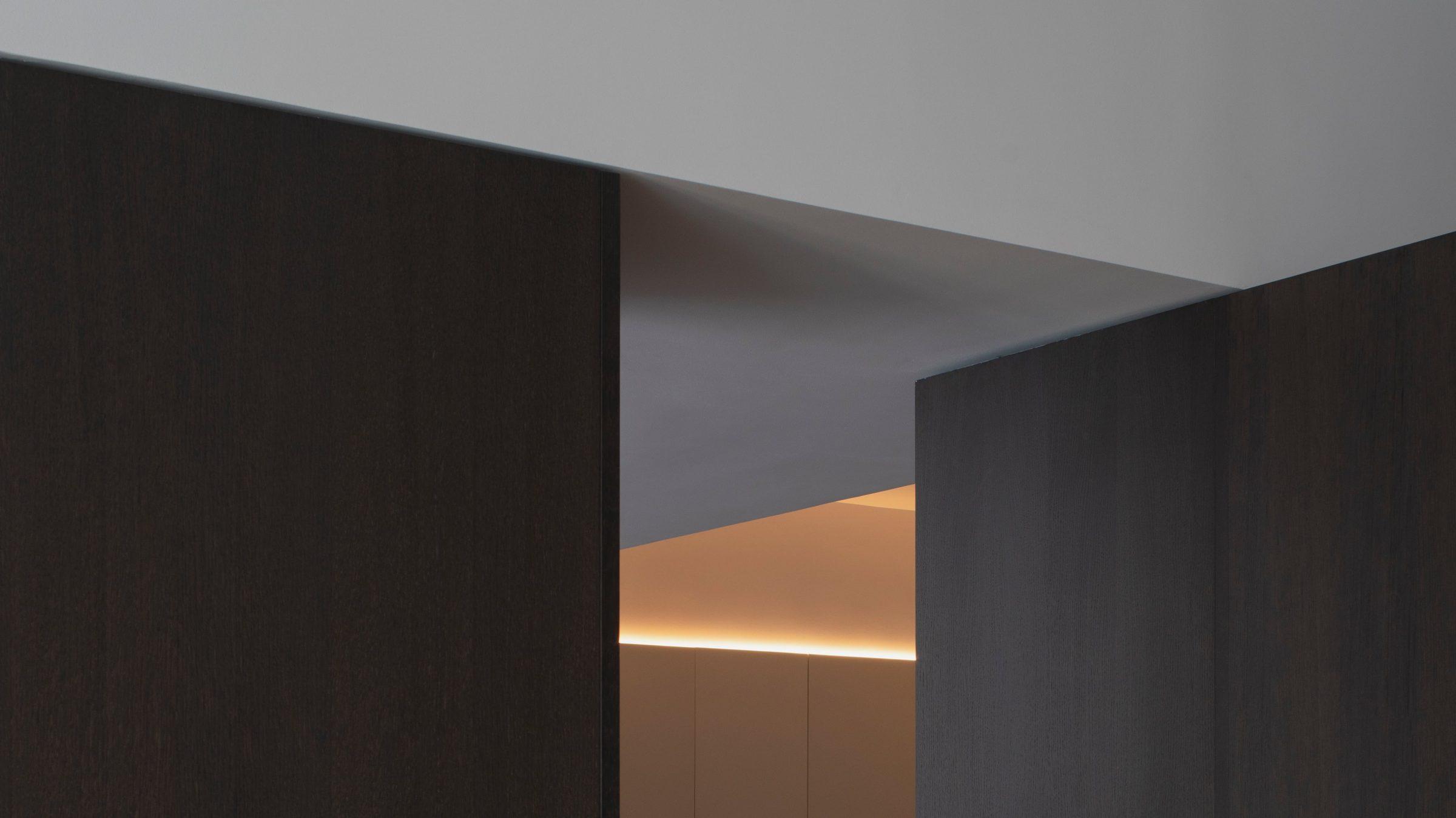 AO17 Apartment — view through dark walnut wardrobes to the warm corridor beyond