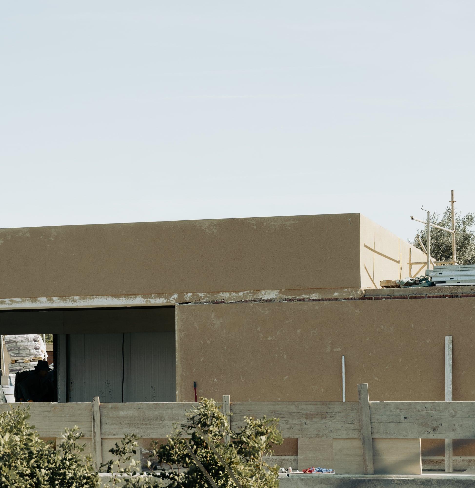 Lime-rendered volume under construction with preserved olive, Bunker House, Ibiza